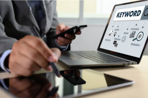 Business professional using a smartphone, tablet, and laptop displaying keyword research tools, highlighting SEO strategy and digital marketing.